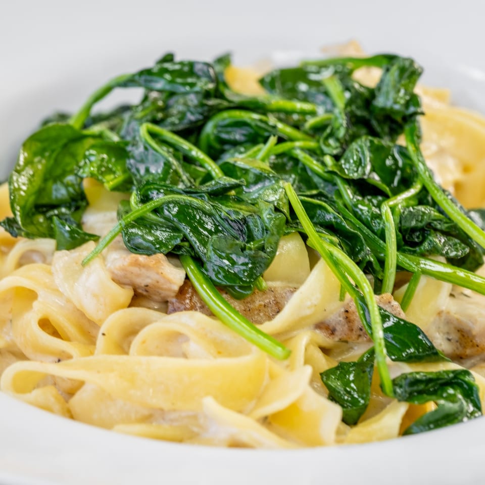 Creamy fettuccine pasta with chicken and fresh spinach in a white bowl.