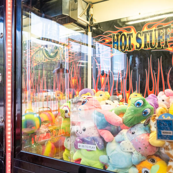 A claw machine filled with colorful plush toys, featuring a "Hot Stuff" graphic with flames.