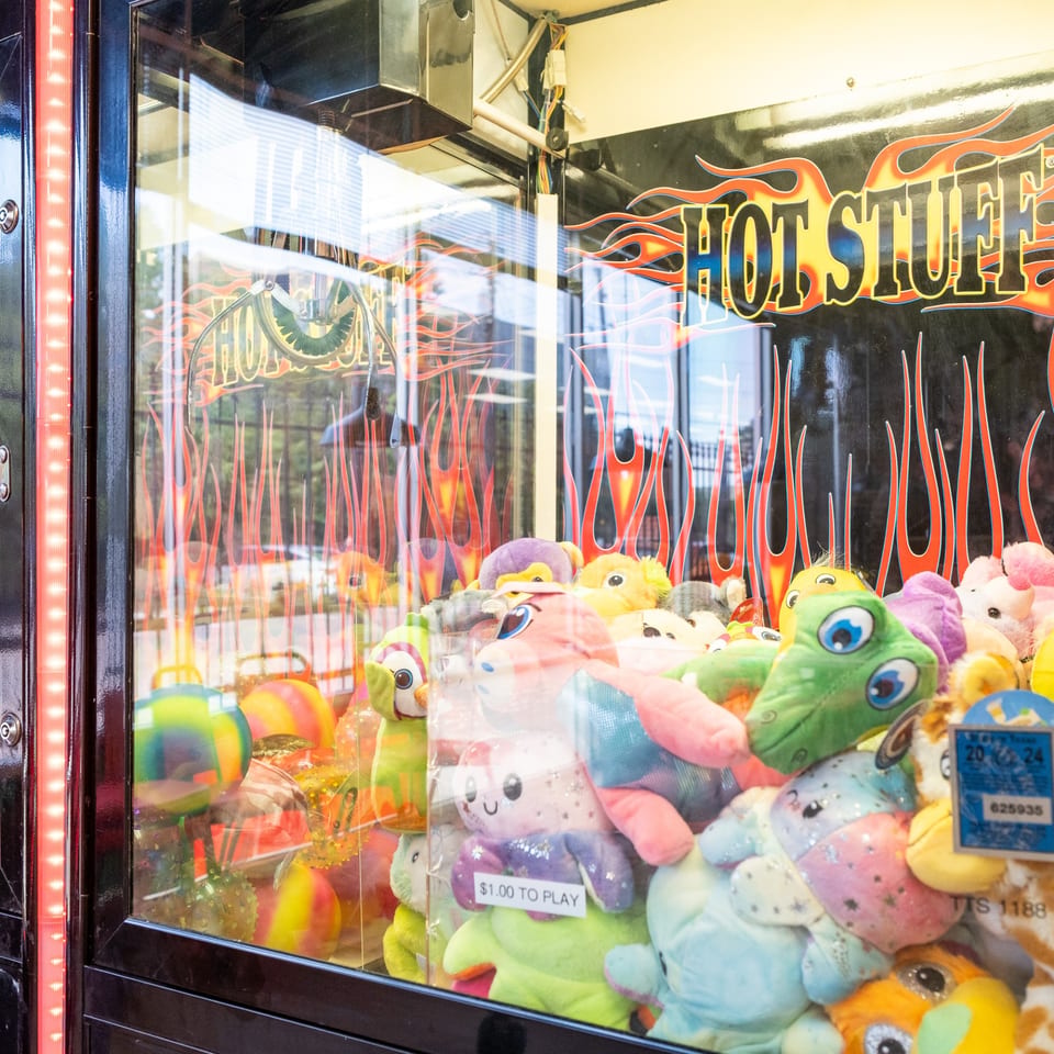 A claw machine filled with colorful plush toys, featuring a "Hot Stuff" graphic with flames.