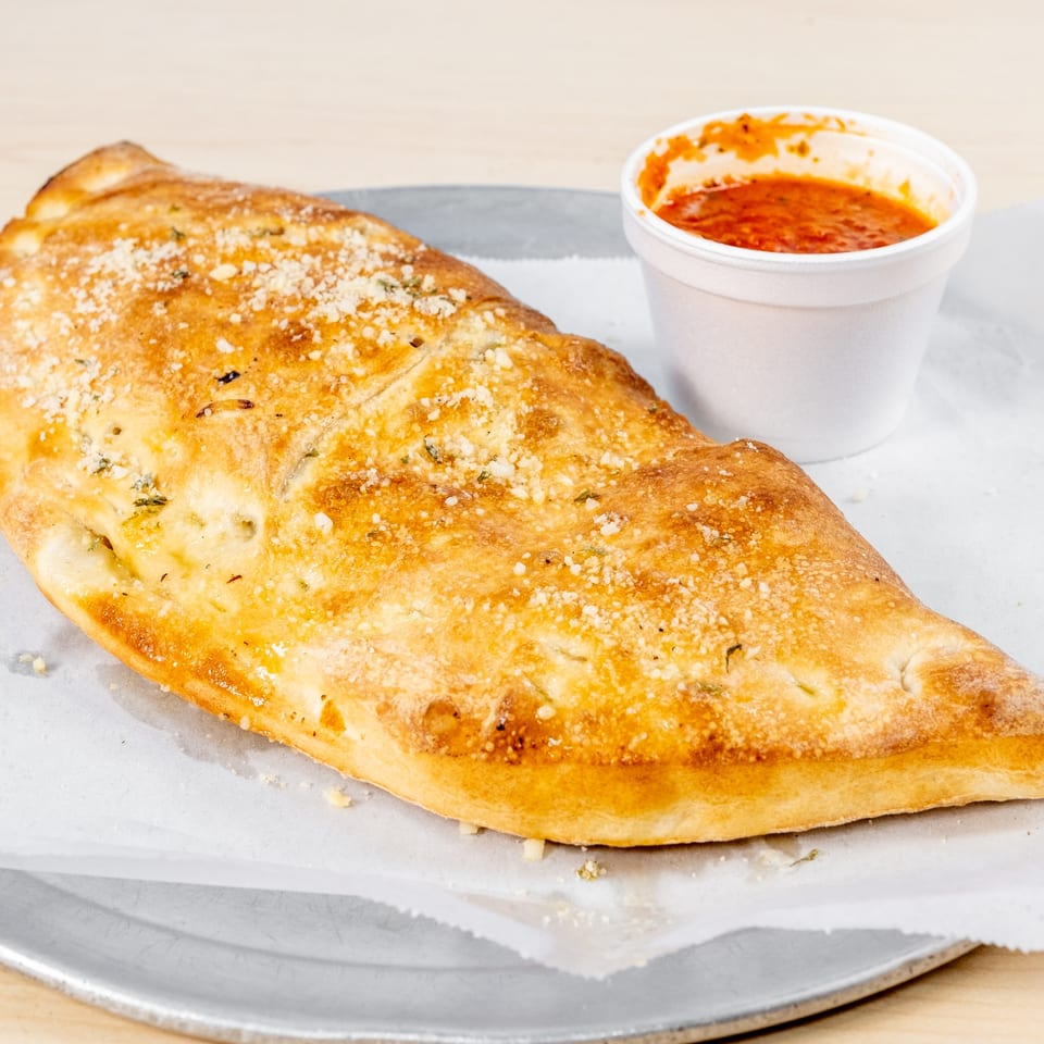 Golden-brown calzone sprinkled with parmesan cheese, served with a side of marinara sauce.