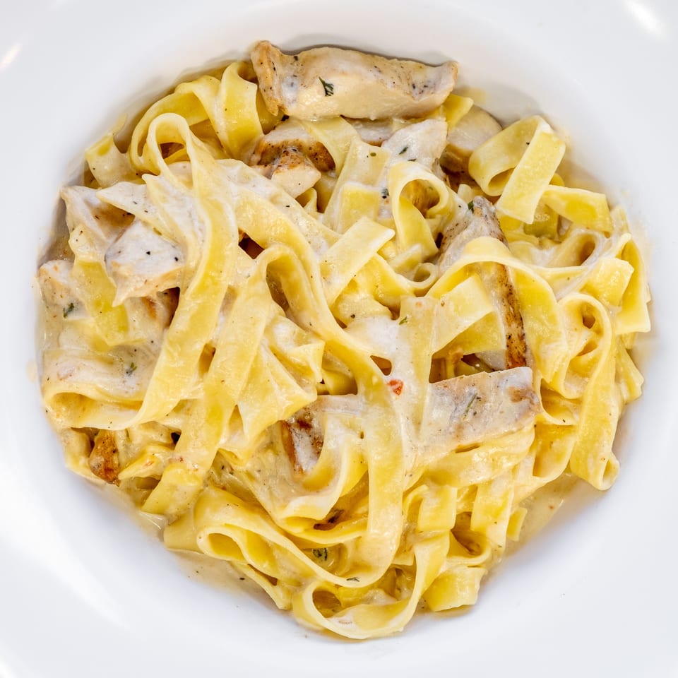 Creamy fettuccine alfredo with chicken and herbs, served in a white bowl.